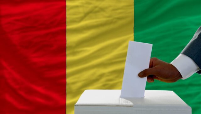 man voting on elections in front of national flag of guinea