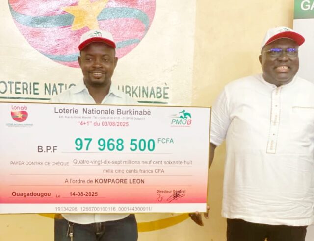 Léon Compaoré avec son chèque en compagnie du représentant du directeur général de la LONAB